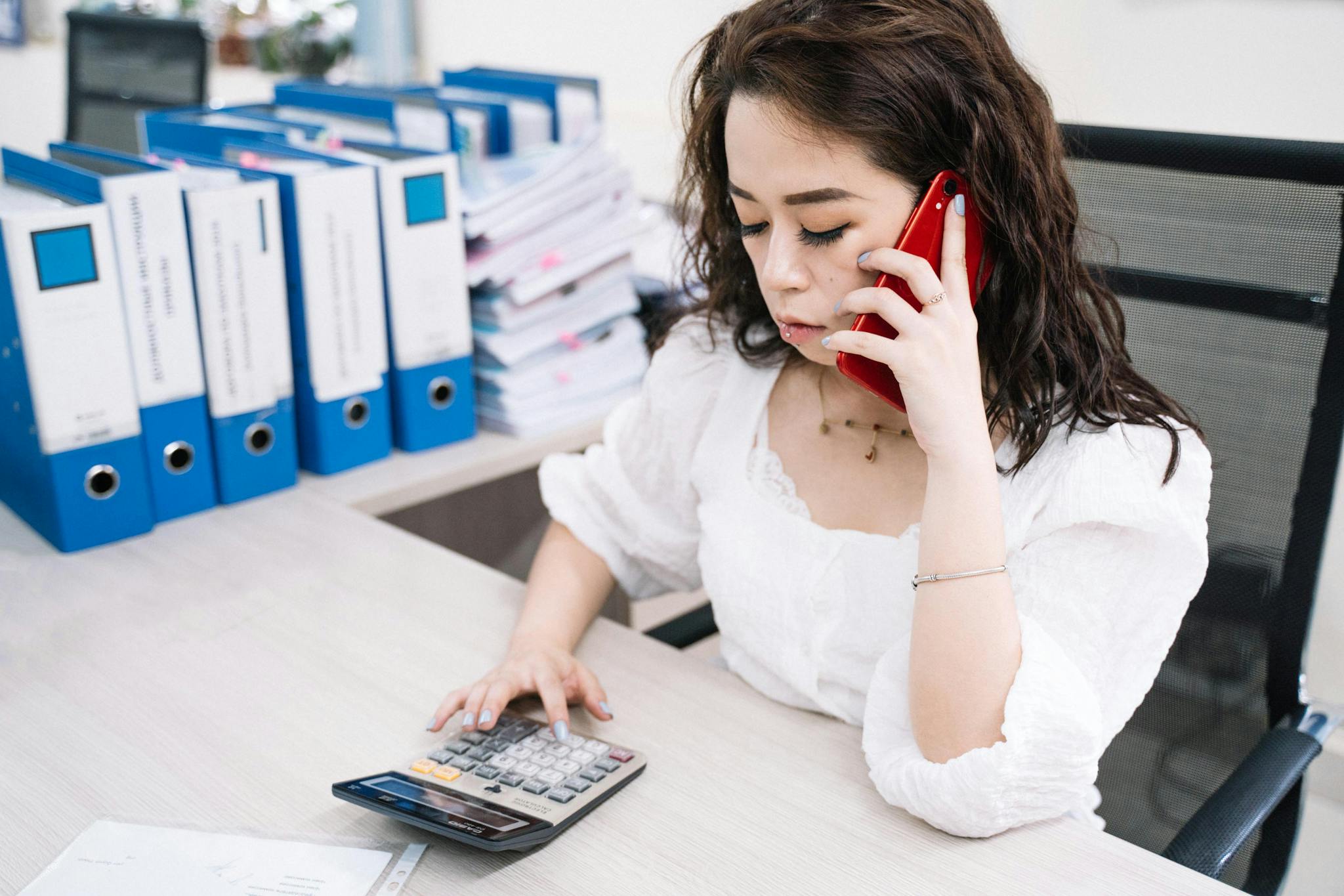 Businesswoman Multitasking With Calculator And Cell Phone